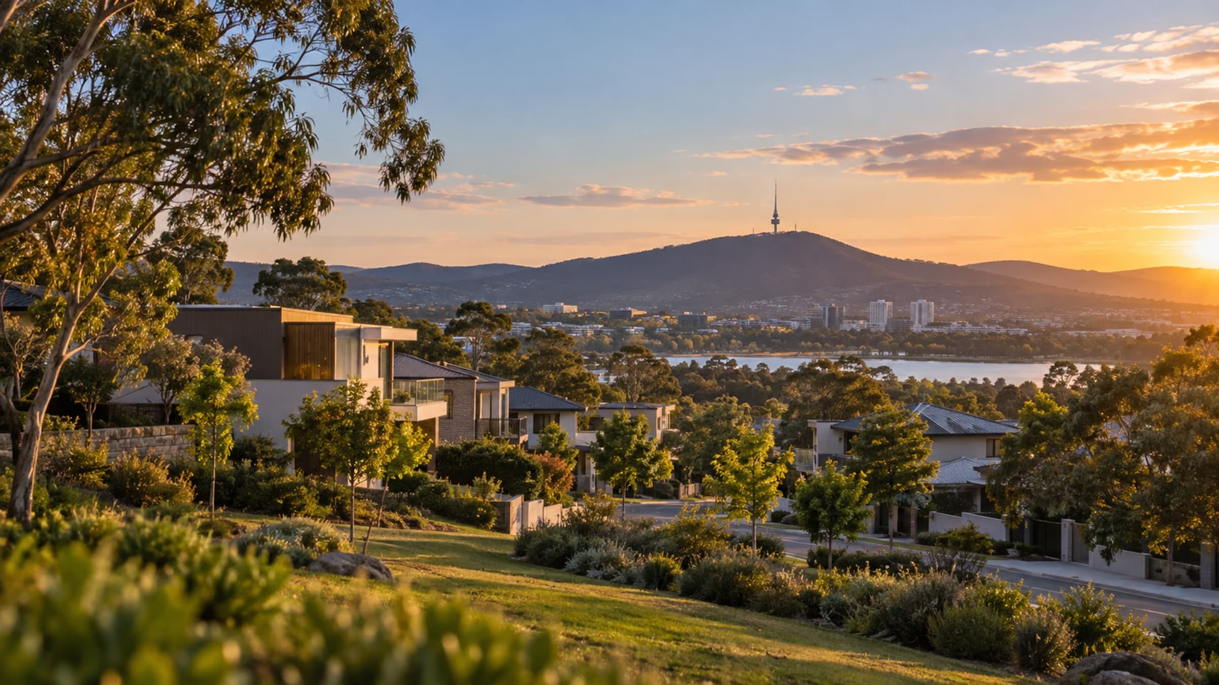 Contemporary homes on a leafy Canberra hillside at sunset, with Lake Burley Griffin, the Brindabella foothills, and the Telstra Tower on Black Mountain in the distance.